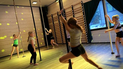 Children doing tricks on pole dance poles at a birthday party. The studio has party lights and a disco ball.